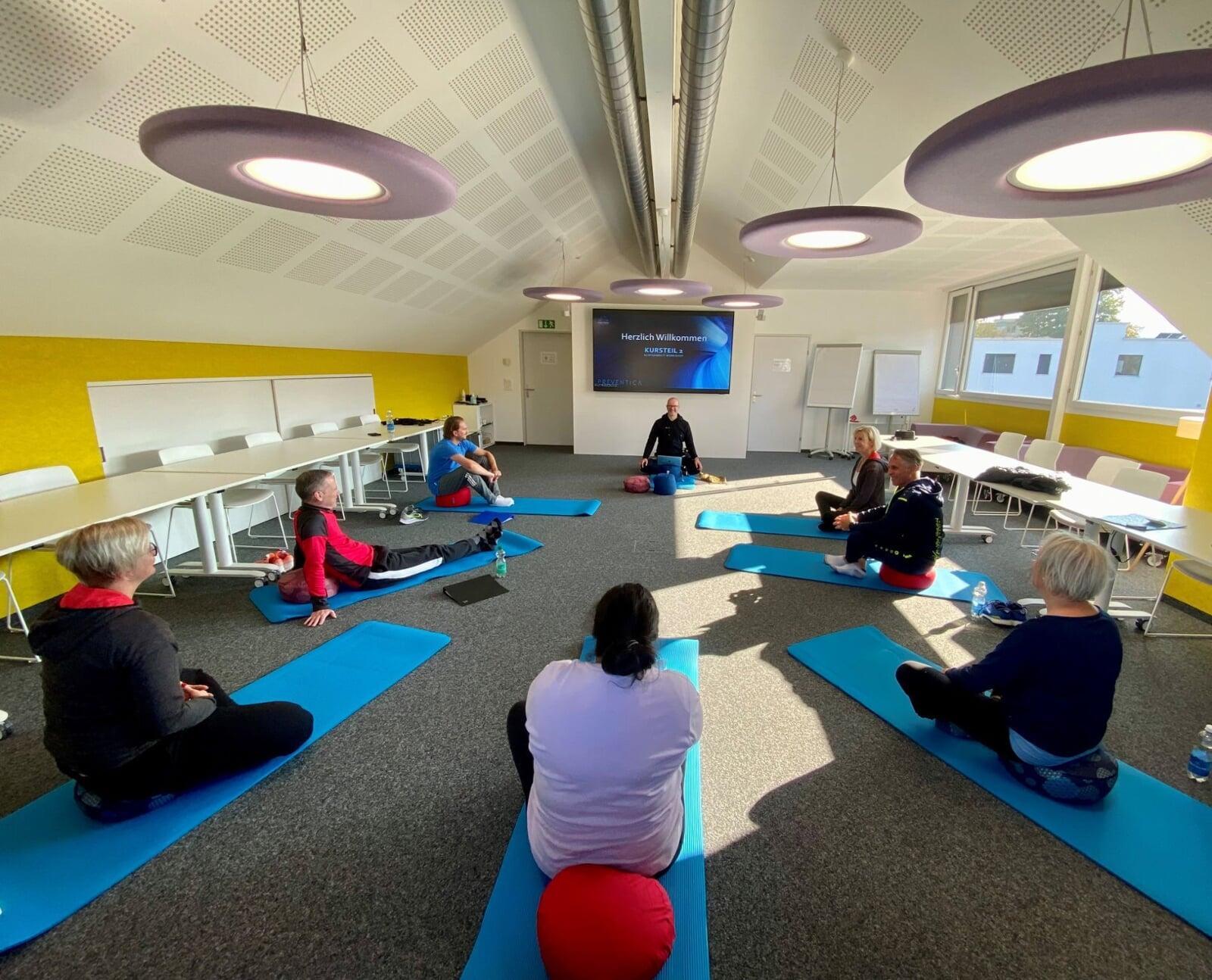 Teilnehmer eines Achtsamkeitstraining sitzen auf Achtsamkeitskissen. Achtsamkeitstrainer Roger Sigrist sitzt vorne in der mitte und leitet die Teilnehmer an