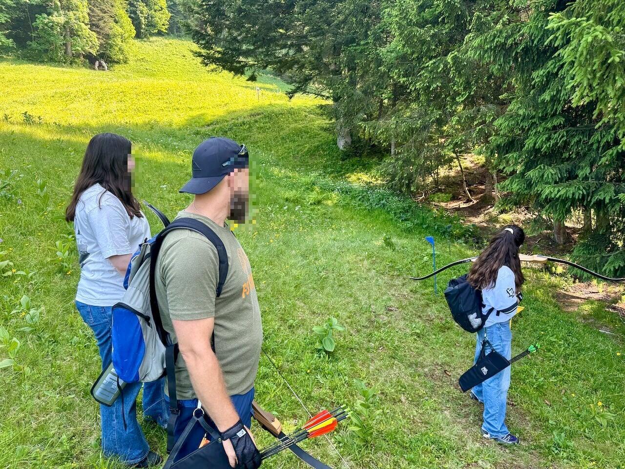 Zwei Jungendliche und eine Betreuungsperson sind draussen in der Natur am Bogenschiessen