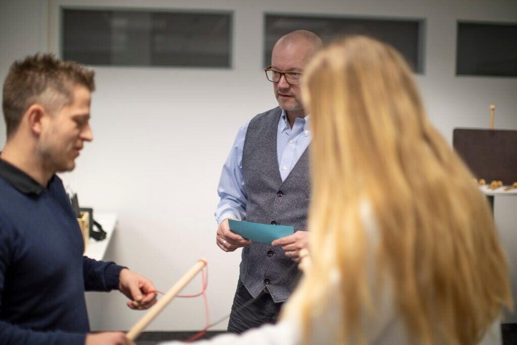3 Personen in einem Raum, machen ein Training. Roger Sigrist im Hintergrund