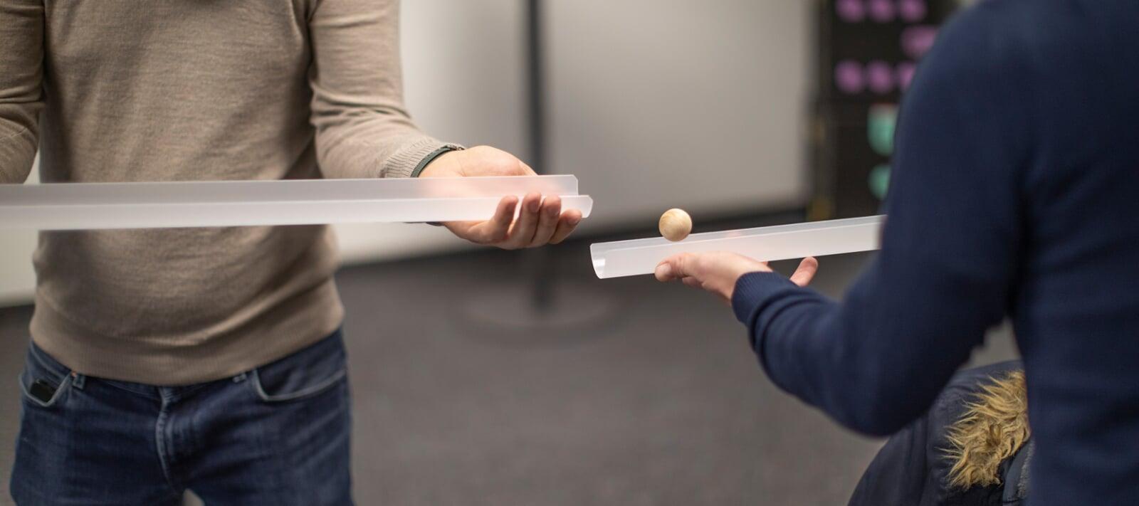 2 Personen halte eine Pipelin in der Hand und eine Kugel springt von der einten Röhre zur anderen