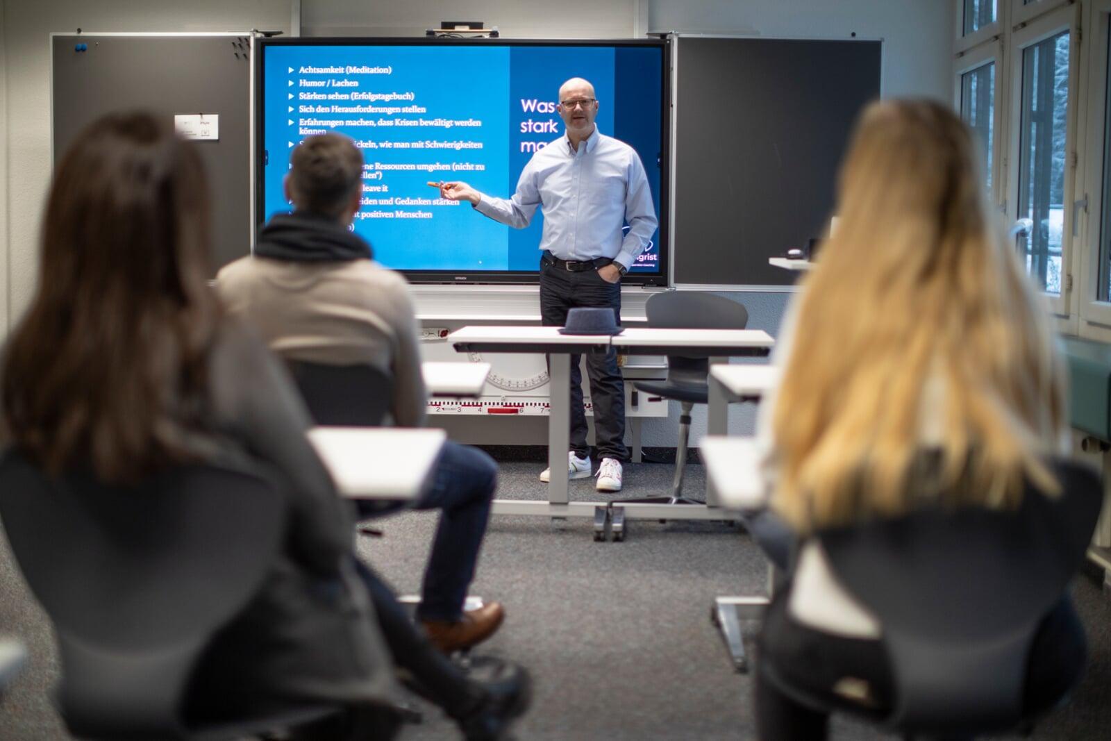 Trainer Roger Sigrist, referiert in einem Schulungsraum vor einem grossen Monitor 