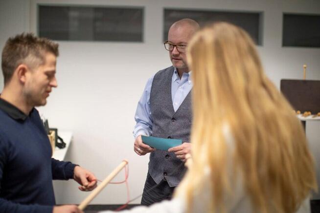 3 Personen in einem Raum, machen ein Training. Roger Sigrist im Hintergrund